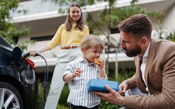 Happy young family with a small child smiling and relaxing while waiting for their electric car to finish charging.