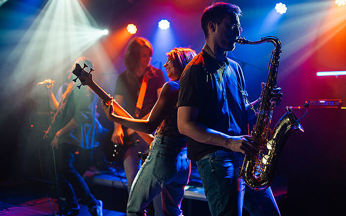 Live music band performing on stage under colorful lights, with musicians playing instruments and creating an energetic concert atmosphere.