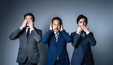 Three businessmen in suits, each covering either their eyes, ears or mouth with their hands, symbolizing the concept of &ldquo;see no evil, hear no evil, speak no evil&rdquo; in a corporate setting.