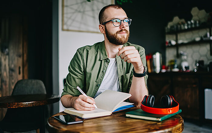 Bearded man sitting in a stylish caf&eacute;, writing ideas in a notebook.