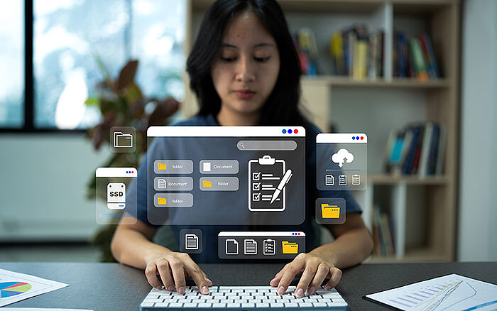 Person typing on a keyboard to download files from a database or document management system, with digital folder icons representing online data access.