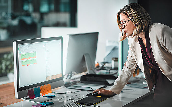 Businesswoman in an office reviewing a schedule or project plan on a computer screen.
