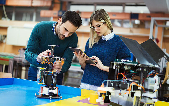 Two young students working together on a robotics project, assembling components in a classroom or lab environment.